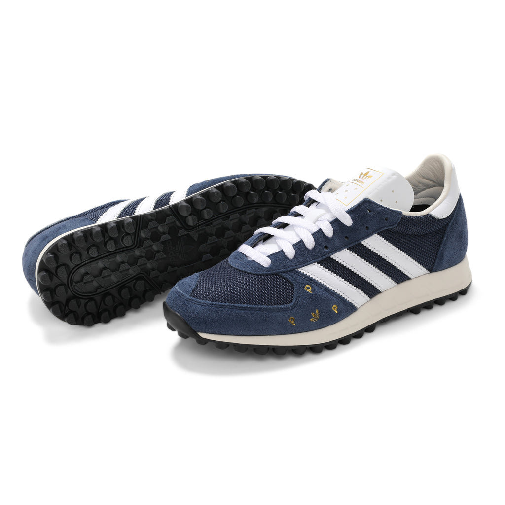 A pair of blue ADIDAS X POP TRADING CO. TRX VINTAGE NAVY/WHITE trainers with white soles.