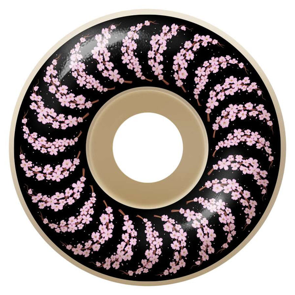 A donut-shaped object against a black background, showcasing the SPITFIRE F4 YUTO CHERRY BLOSSOM CLASSICS 99D 53MM spiral pattern decorated with pink cherry blossoms.