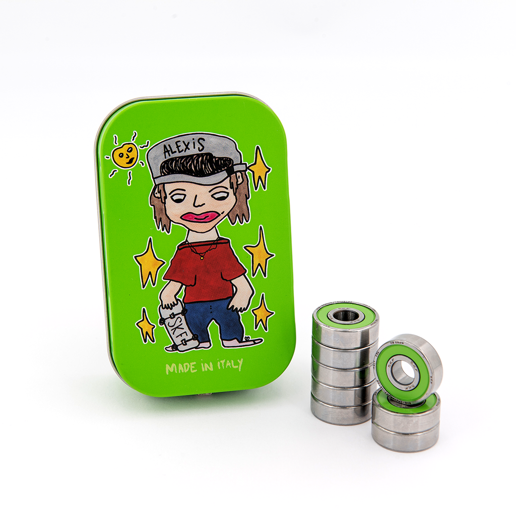 A green rectangular tin with a cartoon drawing of a person wearing a cap on the lid, labeled "SKF Alexis". Next to the tin are two stacks of high quality silver ball bearings with green-colored centers, part of the SKF Alexis Signature Bearing Kit.