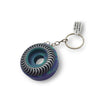 The SPITFIRE KEYCHAIN SWIRL PURPLE / TEAL features a 42mm wheel-shaped pendant with a purple and teal swirl design, accented by a black and white striped optical illusion edge.