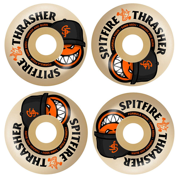 Four beige 54mm SPITFIRE X THRASHER F4 THE CITY RADIAL FULL 99D wheels feature a grinning cartoon face in a black cap with orange details, with “Spitfire Formula Four” and “Thrasher” text on the edge.