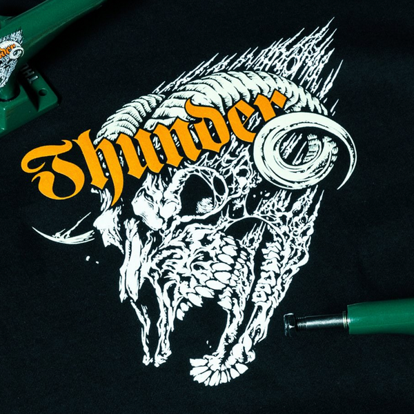 The DELUXE THUNDER SCREAMING SHADOWHORN TEE BLACK features a roaring horned skull graphic with bold yellow "Thunder" text and green metal accents on soft 100% cotton for comfort and style.