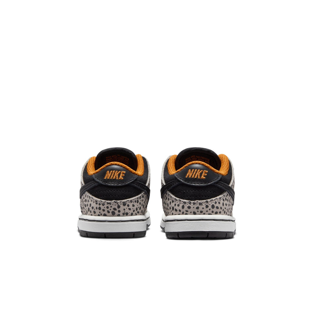 Rear view of a pair of NIKE SB DUNK LOW PRO ELECTRIC TD PHANTOM/BLACK sneakers with a leopard print design, orange inner lining, and white soles. The Nike logo is visible on the black heel. Perfect for toddlers ready to rock skateboards in style.