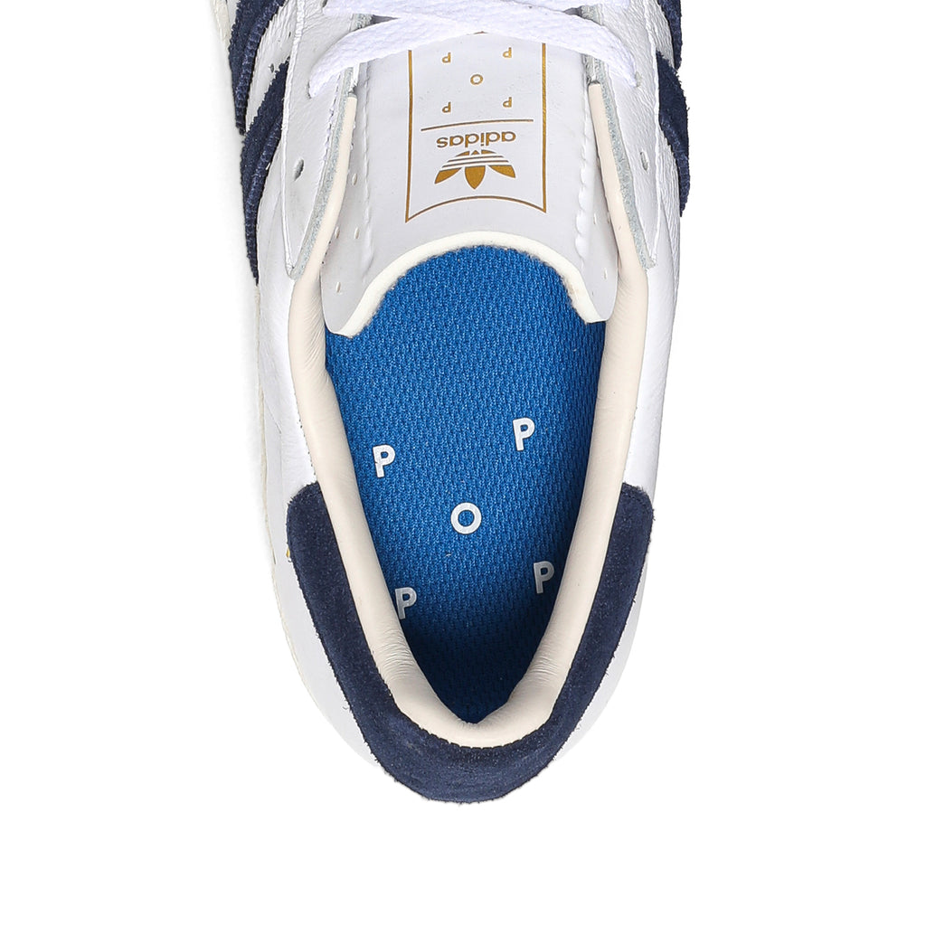 A white and blue ADIDAS X POP TRADING CO. SUPERSTAR ADV shoe with a blue sole, perfect for fans of the New England Revolution.