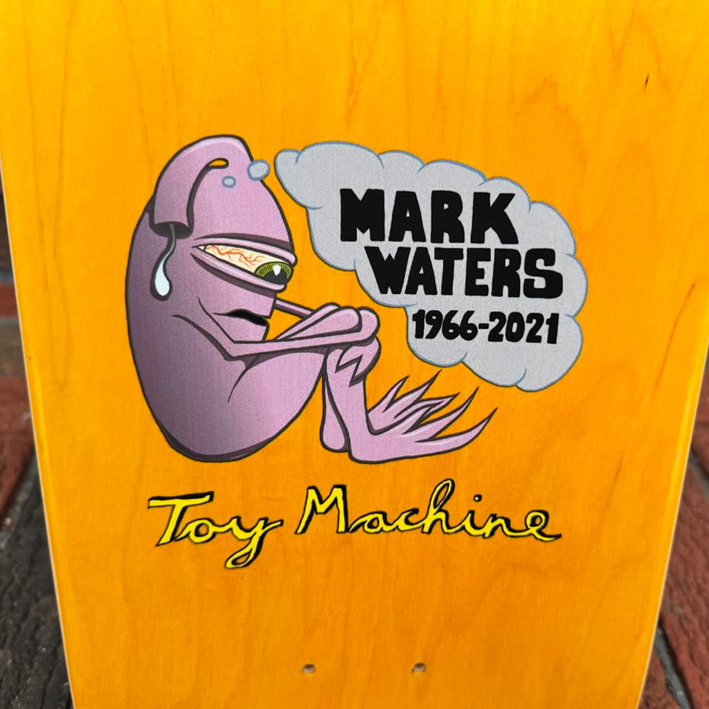 The Toy Machine x Skate Shop Day Mark Waters skateboard deck by Ed Templeton for Deluxe features a purple creature with the tribute "Mark Waters 1966-2021." It's an ideal piece to celebrate Skate Shop Day.