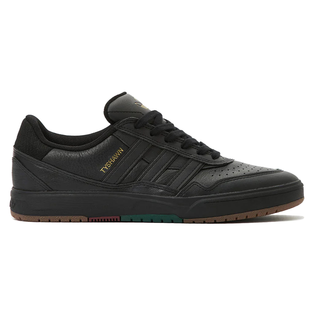 A black skateboarding shoe with a gold "TYSHWN" label, black midsole, and a brown outsole featuring subtle colored accents. These ADIDAS TYSHAWN 2 BLACK / BLACK / GUM sneakers, inspired by Tyshawn Jones, are perfect for any streetwear enthusiast.