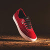 The VANS Skate Curren Caples Red/White sneaker with white soles, black laces, and POPCUSH insoles is shown against a dark background, angled as if floating above a textured surface.