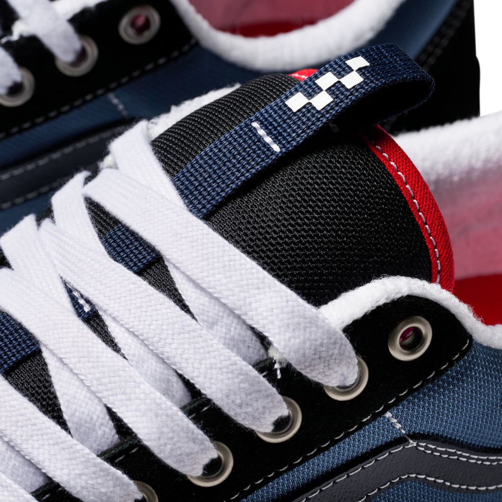 Close-up of VANS SKATE OLD SKOOL 36+ NAVY / RED sneakers with white laces, blue and black fabric, red interior, and a checkered loop on the tongue. Enhanced with DURACAP technology, they offer durability and style for enthusiasts.