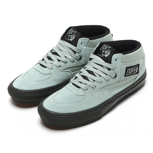 The VANS SKATE HALF CAB GREY OLIVE / BLACK are mid-top suede sneakers featuring a light gray upper, black soles, white laces, and black tongue and side labels—a classic, durable Vans skate shoe designed for peak performance.