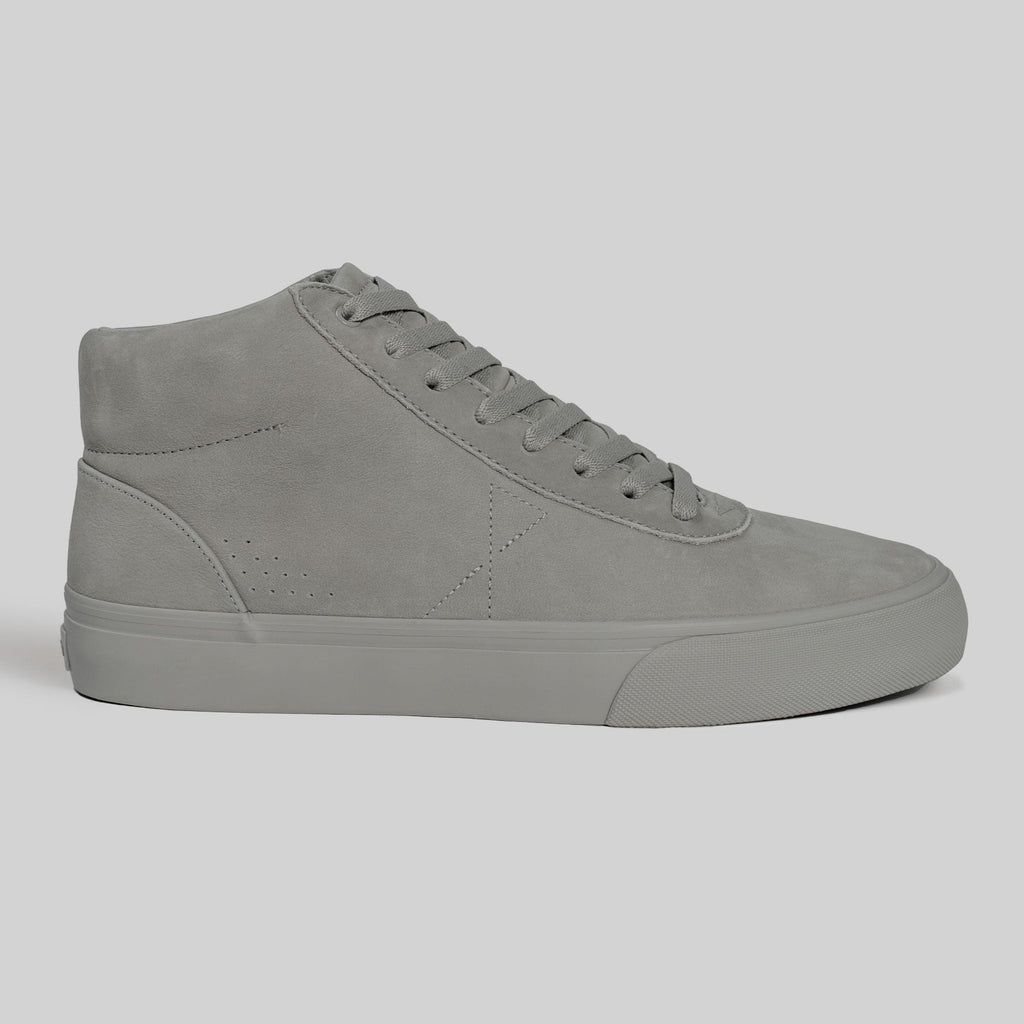 A side view of the CHAPTER MID | STONE FG NUBUCK high-top sneaker by WARSAW LTD highlights its skate-inspired style, featuring grey nubuck and laces against a plain light background.