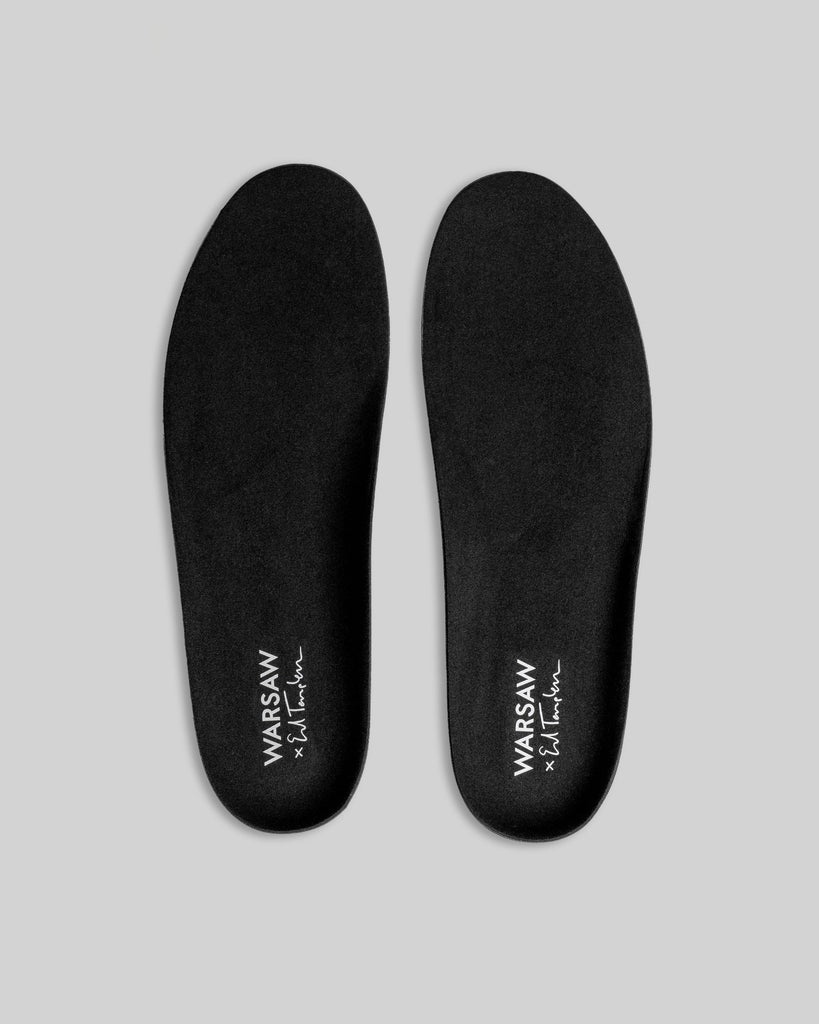 A pair of black WARSAW LTD STRANGER SLIP-ON | TEMPLETON COLLAGE insoles featuring "WARSAW x SAI FRANK" in white on the heel, displayed side by side on a light gray background—ideal for skate-inspired footwear fans.