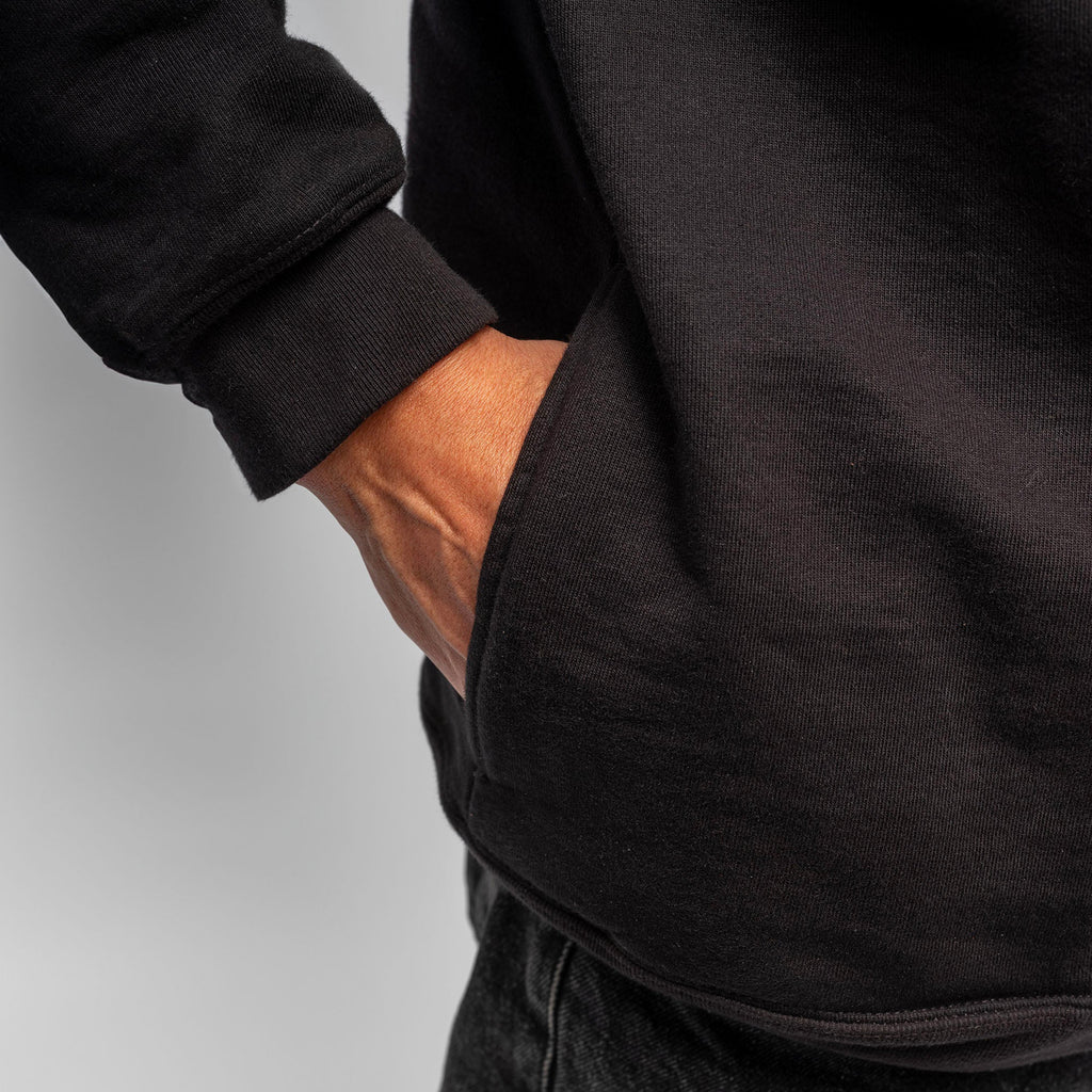 A person wearing the WAR SAW X TEMPLETON PROFILE CREWNECK in black and dark jeans, with their right hand in the hoodie pocket.