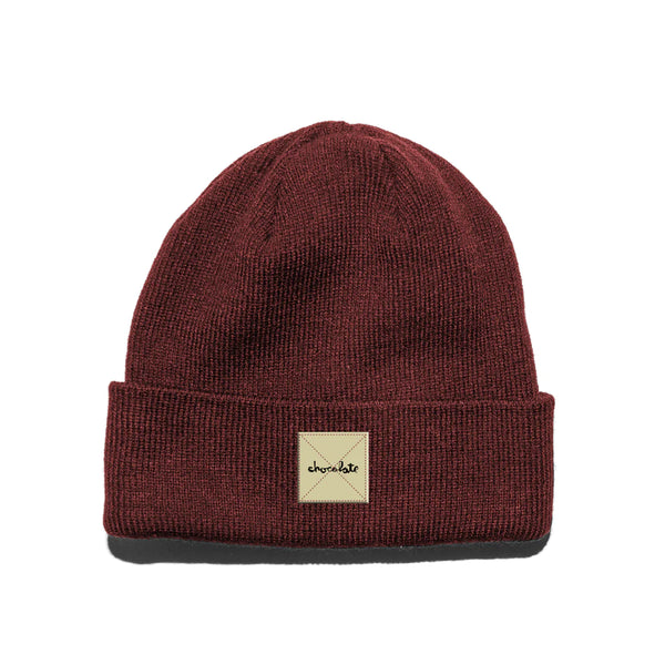 A CHOCOLATE WORK BEANIE BURGUNDY with a black patch on it.