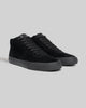 The WARSAW LTD CHAPTER MID | BLACK / BLACK features black pig suede high-top sneakers with black laces and rubber soles, designed for comfort and durability, shown on a plain gray background.