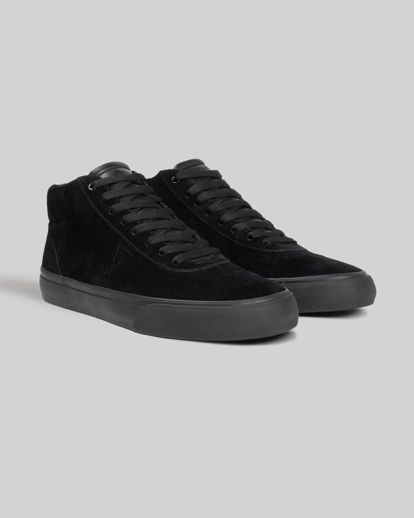 The WARSAW LTD CHAPTER MID | BLACK / BLACK features black pig suede high-top sneakers with black laces and rubber soles, designed for comfort and durability, shown on a plain gray background.