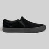 The STRANGER SLIP-ON | BLACK / BLACK by WARSAW LTD is a black genuine pig suede slip-on sneaker with a matching rubber sole and subtle stitching, shown against a plain gray background.