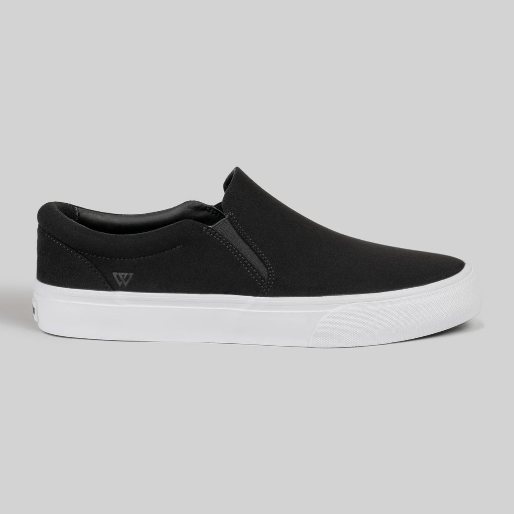 The WARSAW LTD STRANGER SLIP-ON | BLACK / WHITE SYNTHETIC is a black minimalistic slip-on sneaker with a white rubber sole, showcased against a plain light gray background.