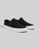 The WARSAW LTD STRANGER SLIP-ON in black/white synthetic features a minimalistic silhouette and white rubber soles, displayed on a plain grey background.