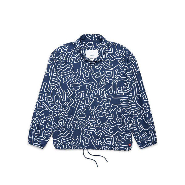 The HERSCHEL X KEITH HARING VOYAGE COACH by HERSCHEL is a navy blue jacket featuring white Keith Haring-inspired abstract line art, long sleeves, a collar, front buttons, and an adjustable drawstring hem.
