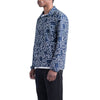 A person wearing the HERSCHEL X KEITH HARING VOYAGE COACH shirt in blue with a white abstract line pattern, black pants, and a white undershirt, shown from the side against a white background. Brand: HERSCHEL.