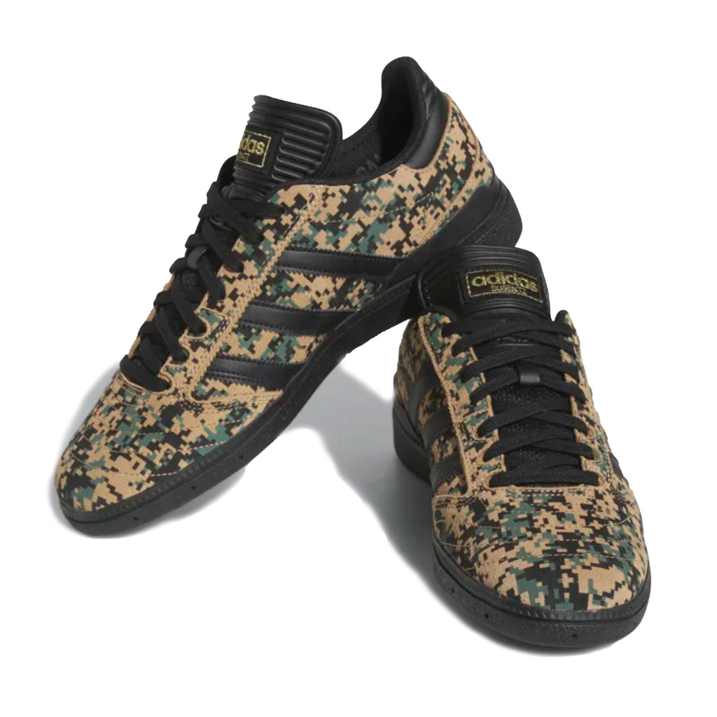 A pair of ADIDAS BUSENITZ BLACK / CARDBOARD / GOLD sneakers with camouflage print on them.