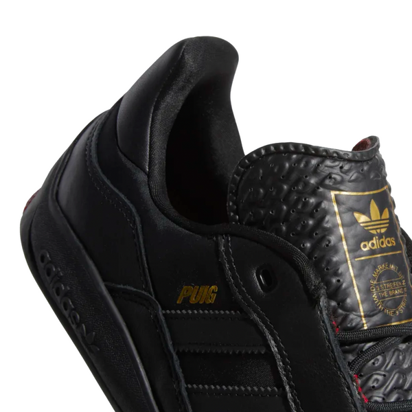A pair of black Adidas Puig Core Black/Scarlet sneakers on a white background.