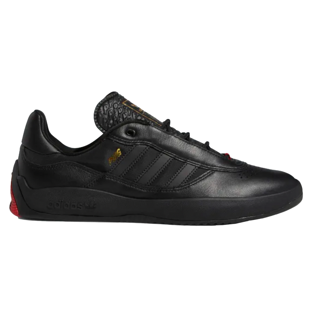 A black ADIDAS Puig Core sneakers with a red sole.