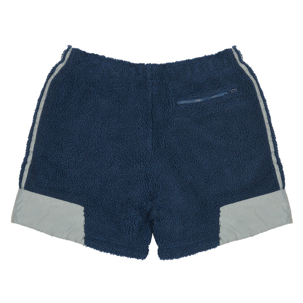 The ADIDAS X BLONDEY SHERPA SHORT MINERAL BLUE by ADIDAS features mineral blue sherpa fabric, light gray side and hem panels, plus a zippered back pocket.