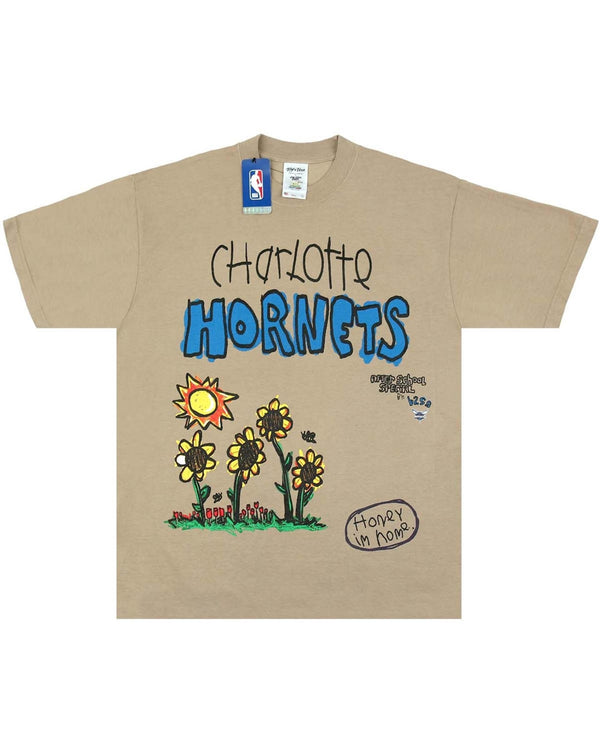 Oatmeal-color NBA HORNETS TEE from AFTER SCHOOL SPECIAL, featuring the text "Charlotte Hornets," floral designs, a sun, and a bee illustration with the phrase “Honey in home.” This Premium Heavyweight Garment Dyed Tee includes an NBA logo tag on the collar.