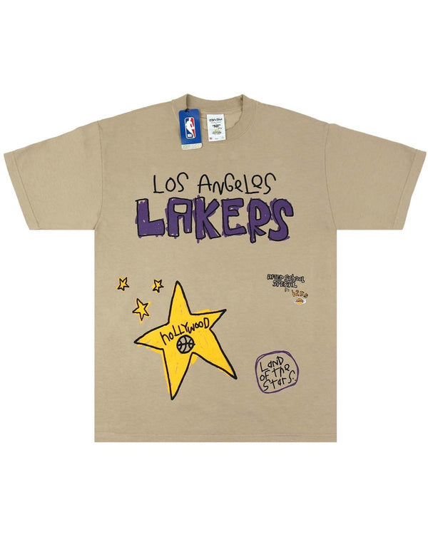 The AFTER SCHOOL SPECIAL A.S.S. X SHAKA WEAR X NBA LAKERS TEE OATMEAL features a Los Angeles Lakers design, showcasing purple and yellow graphics including stars, the word "Hollywood," and "Land of the Stars" text. This Premium Heavyweight Garment Dyed Tee is complete with an NBA logo tag on the collar.