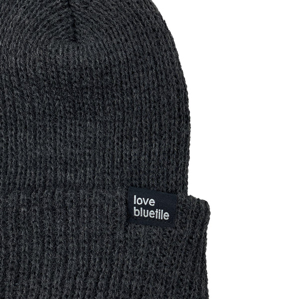 A dark grey BLUETILE Love Always knit beanie with a label on it.