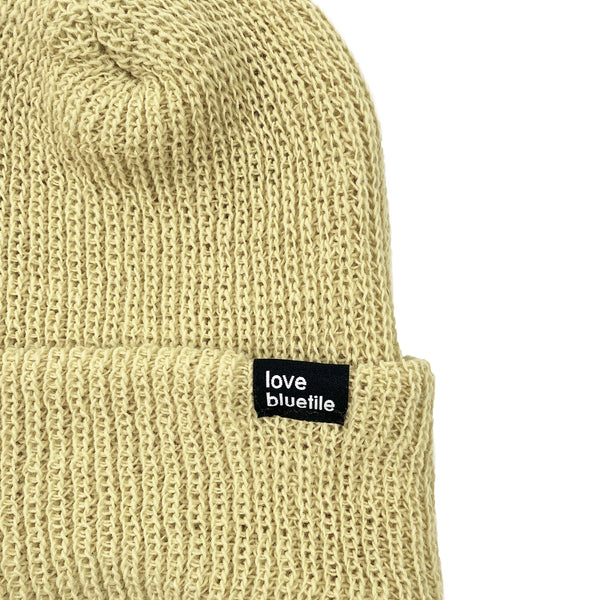 A yellow BLUETILE LOVE ALWAYS KNIT BEANIE VEGAS GOLD with a black label, perfect for those chilly days.