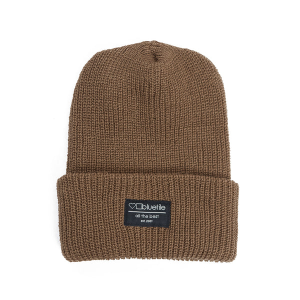A BLUETILE SURPLUS BEANIE COYOTE BROWN with a label on it.