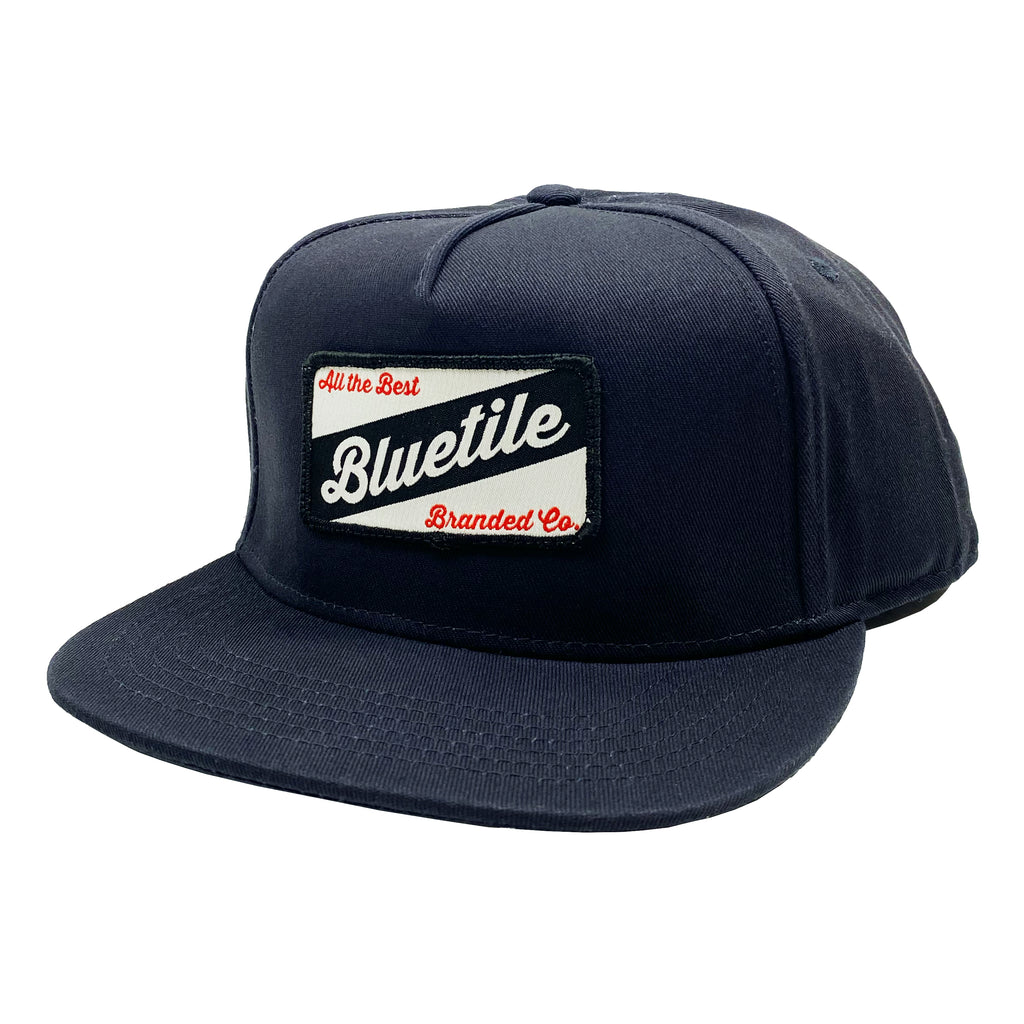 A navy snapback hat with the word BLUETIE on it by Bluetile Skateboards.