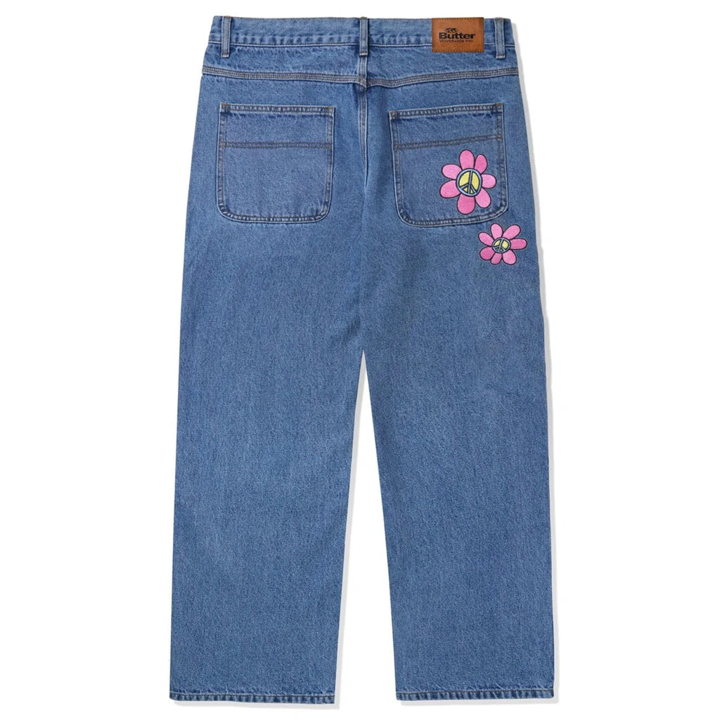 A pair of BUTTER GOODS FLOWER DENIM JEANS WASHED INDIGO from Butter Goods with pink flowers on the side.