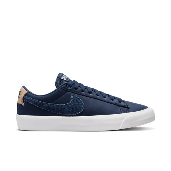 Side view of a NIKE SB BLAZER LOW PRO GT MIDNIGHT NAVY / WHITE sneaker with a white sole. The shoe features a large navy swoosh logo on the side and a beige accent on the heel, perfect for hitting the skateboards.
