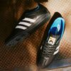 A pair of black and blue ADIDAS GINO SAMBA ADV RYR BLACK / WHITE sneakers, specifically on a metal surface.