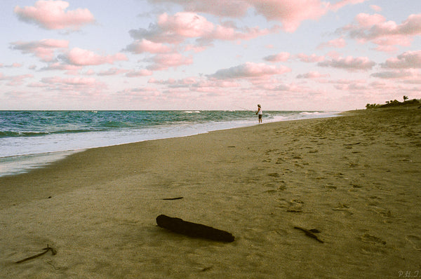A person walking on a beach at sunset, captured in a mesmerizing photo print by Bluetile Skateboards' product, Peace In Isolation by Philip Taylor.
