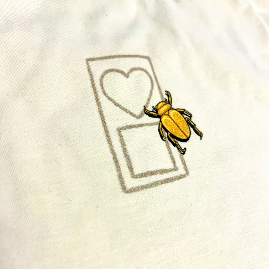 A yellow beetle on a white t-shirt, inspired by the vibrant hues of the Bluetile Pharaoh Mummy Desert Sand, offered by Bluetile Skateboards.