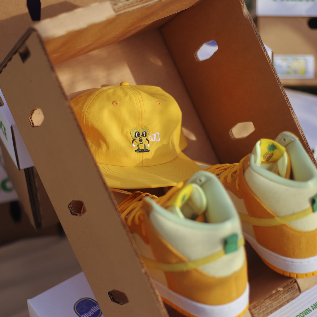 A pair of BLUETILE Smoke Squares Nylon 6 Panel Yellow shoes and a yellow hat in a cardboard box.
