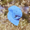 A BLUETILE blue hat hanging from a tree branch.