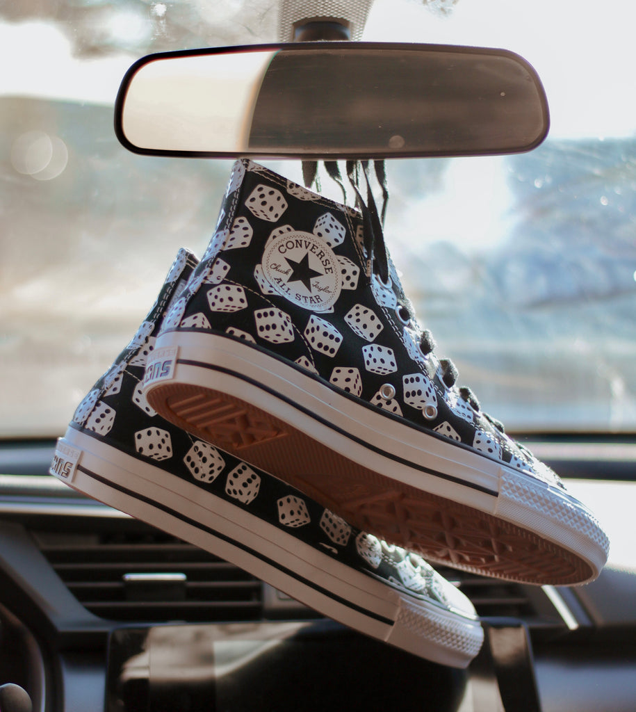 A pair of CONVERSE CONS CTAS PRO HI DICE BLACK / WHITE shoes hanging from the dashboard of a car.