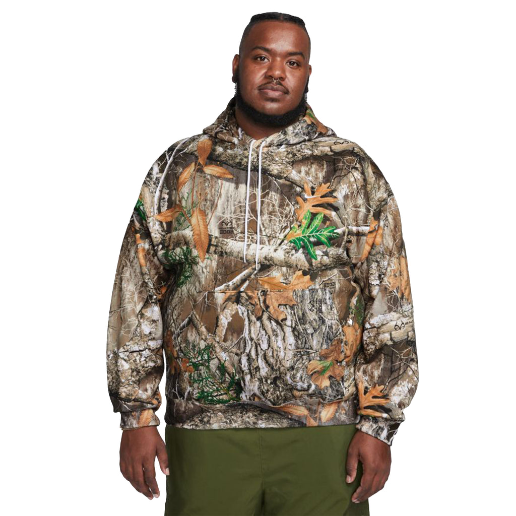 A man wearing a Nike SB x Realtree® Fleece Allover Camo Hoodie and green pants.