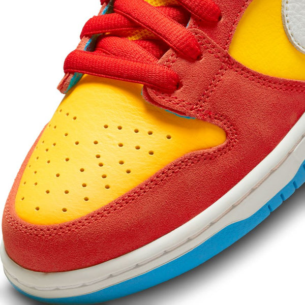 Close-up of the NIKE SB DUNK LOW PRO "BARTS" HABANERO RED sneaker by Nike, showcasing a Habanero Red suede toe cap, yellow leather perforated toe box, red laces, and part of a blue and white sole.