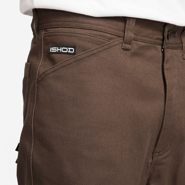 Close-up view of durable NIKE SB ISHOD Pants in brown, featuring a small black and white "ISHOD" label above the pocket.