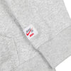 Close-up of the Nike SB OSKI Orange Label Hoodie Grey, featuring a white label with red and gray Nike SB branding and "OSKI Orange Label" text sewn near the hem.