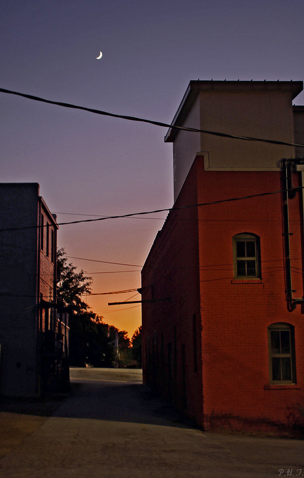 A red building with a Transitions by Philip Taylor print of a crescent moon in the sky.