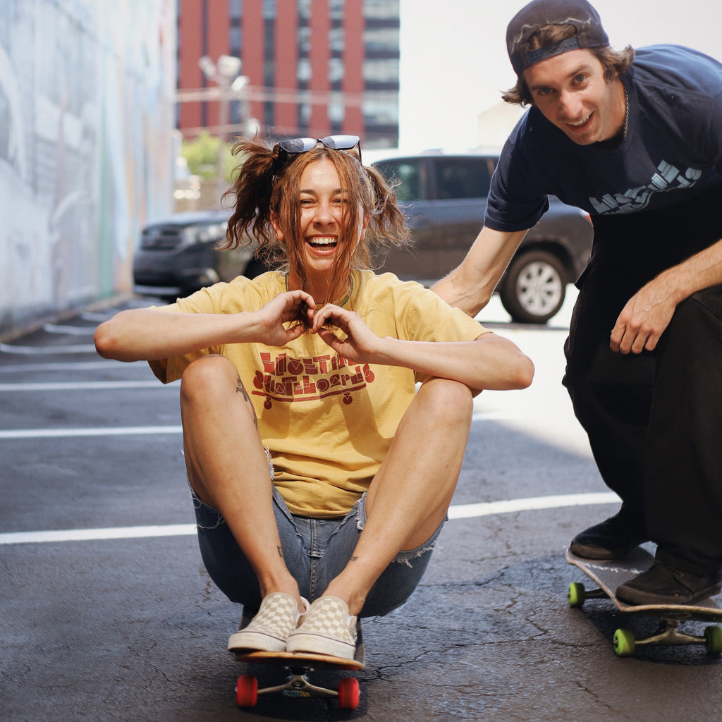 A couple of people that are sitting on a skateboard wearing BLUETILE BASIC SHAPES TEE ARTISAN GOLD.