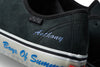 A close up of a black VANS shoe with blue writing on it.