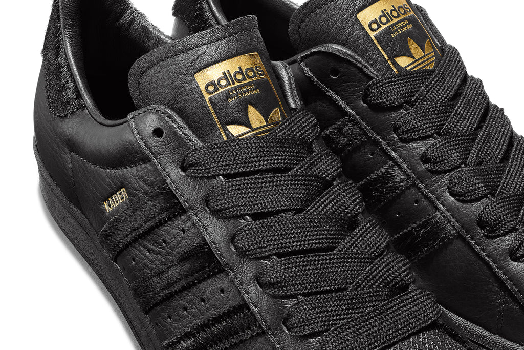 The ADIDAS KADER SUPERSTAR CORE BLACK / CORE BLACK with gold accents.